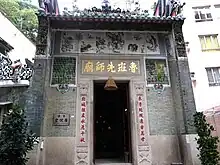 The exterior of a temple, with a large door flanked by Chinese characters. Other urban buildings can be seen in the background.