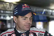 A man in his early forties sporting a navy blue baseball cap with sponsors' logos and headphones to hear his team over the radio