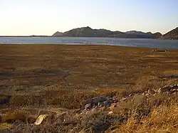 A photo of a dry lakebed with some ruined foundations.