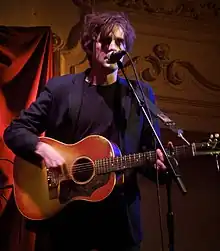 Crook singing into a microphone while playing the acoustic guitar