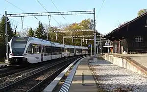 White train on double track passing station