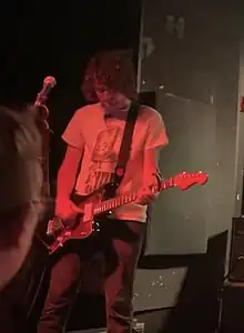 Lenderman playing guitar under dark red lighting