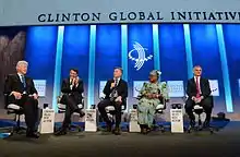 Macri seated onstage with Bill Clinton, two other men and a woman