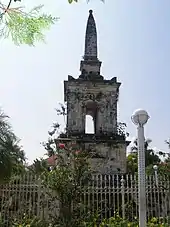 Tall stone memorial with spire and surrounded by a metal fence.