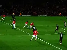 A wide shot of a football match with Manchester United in red in possession against Lyon in black.