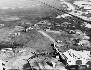 Airfield with several biplanes and hangar marked "MASCOT", photographed from overhead