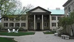 A stone and cream colored building with a green roof and a large portico