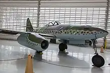 A color photo of a twin engine jet-fighter aircraft standing in a hangar.