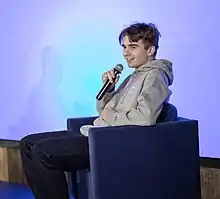 Side view of a smiling Michał Matczak, as he is participating in a panel during a conference