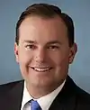 facial portrait of a smiling middle-aged man wearing a dark blue suit with a light blue tie