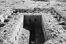 A rubble-strewn rectangular concrete opening with a long thin slot in the middle. More rubble can be seen at the bottom of the shaft in the bottom centre of the photograph