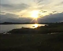 The sun low over the horizon over a body of water surrounded by dark vegetation