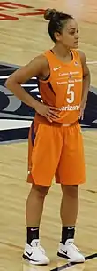 Young woman standing with her hands on hips wearing orange basketball uniform