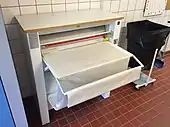 An electric mangle is a chest-high, rectangular cabinet with an opening in the front. From the opening, a long sheet of cloth nearly as wide as the machine spills out into a tray below. Controls at the right of the front face of the machine operate a light which illuminates the opening, and the feed of the cloth in and out of the mangle.