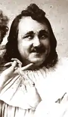 plump middle aged white man with moustache and long dark hair, looking coy