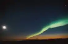 A night sky with the moon on the left and the aurora (northern lights) on the right.