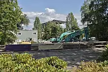 Excavating equipment in a concrete parking lot, behind a fenced off courtyard