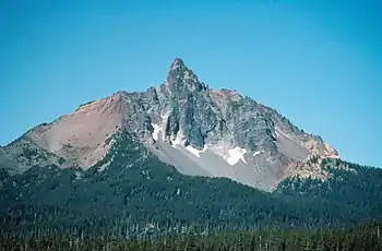 An eroded volcanic edifice rises above a forested region