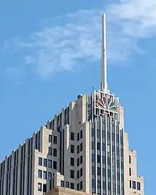 Closeup of the top of an Art Deco-styled skyscraper with the NBC peacock logo