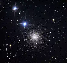 A round cluster of tiny distant stars with two bright bluish stars to the upper left