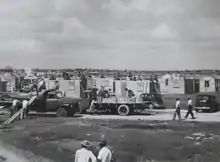 Slightly elevated view of workers constructing an entire neighborhood. The houses are all of similar appearance, with windows and a door.