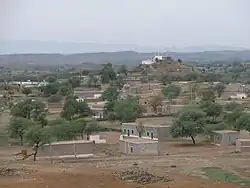 Photograph depicting brick dwellings of the village nestled among hills and low mountains with a large white Masjid situated at top of hill