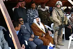 A Marine officer standing with a group of Iraqis, some in suits, some in traditional garb, and some in military uniforms.