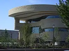 A large curving beige stone building with bands of windows delineating each floor. The curving roof line extends out beyond the building and steps back twice to reach the rest of the structure.