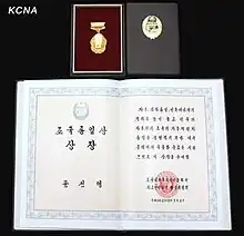 A photograph of the Prize awarded to Moon Sun Myung in 2012. It shows a gold medal depicting the Korean peninsula, and a certificate with calligraphic writing and a seal.