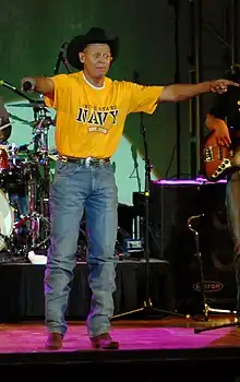 Singer Neal McCoy at the edge of a stage, holding his arms out.