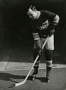 Hockey player dressed in uniform and equipment in a pose with a hockey stick and puck