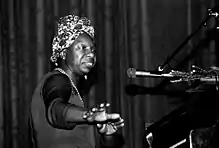 Head and torso of black woman at a piano in front of a microphone wearing a flowered kerchief in her hair