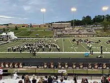 This image shows the North Augusta High School football team running onto a football field through a tunnel. The band can be seen performing in concert arch and there are students running with flags ahead of the team.