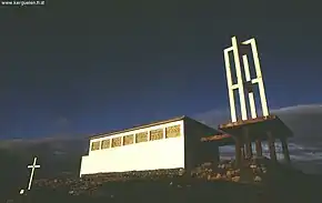 A white concrete church with a skeletal bell tower and thickly leaded stained glass.