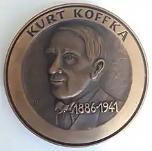 A bronze medallion with an outer ring containing the text "KURT KOFFKA" at the top, containing a central embossed image of a three-quarter face and upper chest of Kurt Koffka looking to the right. Superimposed on the chest and to the left of the midline is the text "1886-1941"