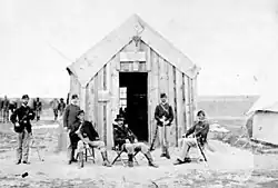 Black and white photo of a group of men in uniforms in front of a wooden building