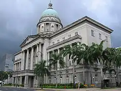 A dome sits atop this building, which is next to a road. The building's large entrance stands at its centre and is fronted with pillars.