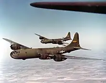 Two large olive-colored aircraft flying over farmland