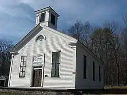 A white building with a square tower on top and black roof photographed from the right and lit by the sun from the left