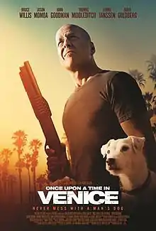 A man holds a shotgun next to a dog in front of a sunrise.