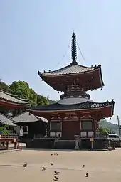 Wooden two-storied pagoda shaped building with a square base and a round upper floor, white walls and red beams.