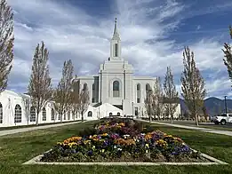 A planted garden in a grounded concrete box is seen in the center, leading to the tall granite parapets of the Orem Utah Temple. On the left, a white tent (from the open house) is seen leading up to the temple entrance.