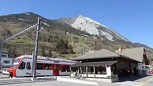 Red-and-white train next to two-story station building