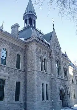 Exterior of a two-story building constructed in Gothic Revival architectural style featuring grey granite bricks and gables with copper roofing