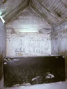 Small stone chamber, its walls inscribed with hieroglyphs and its gabled roof covered with painted stars. At the center is a massive but broken black sarcophagus.