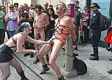 A woman holding a bound man's penis applies electricity to his testicles at Folsom Street Fair. The electricity applied should never be increased suddenly.