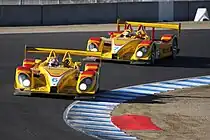 Two bright yellow racing sports cars on a race track taking a left hand corner