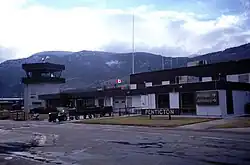 The main terminal building of an airport, with a "Penticton" sign near the entrance, and an "Arrivals" sign pointing to the right, with the same word written in French below it