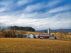 A grouping of farm buildings backdropped by a field, mountains, and the sky.