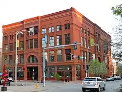 A large four-story red brick building with many windows. The building is on a street corner with the front and one of the sides visible.